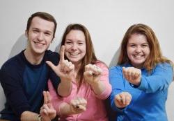 Photo of three students holding up their hands to sign ASL